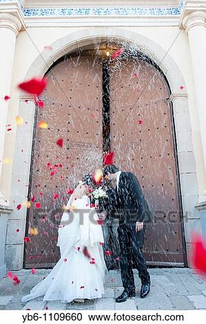 A just married couple coming out of the church with people throwing rice and rose petals to them. View Large Photo Image Stock Image - A just married couple coming out of the church with people throwing rice and rose petals to them.. Fotosearch