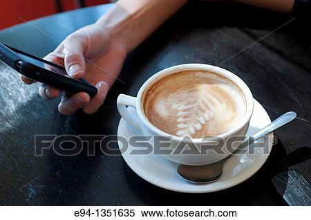 A large coffee cup and a woman's hand holding a mobile phone. View Large Photo Image Stock Photography - A large coffee cup and a woman's hand holding a mobile phone.. Fotosearch