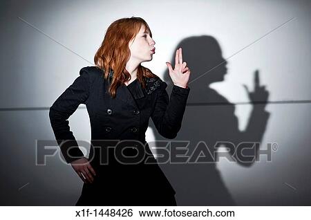 Stock Photograph - A late teen early 20s single woman girl with red hair pointing her fingers like a gun, casting shadow, blowing her lips, UK. Fotosearch