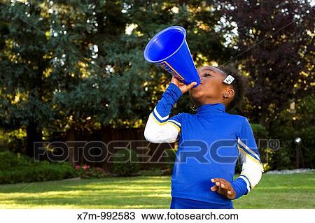 Stock Image - A little black girl dressed as a cheerleader for Halloween yelling through a megaphone. Fotosearch