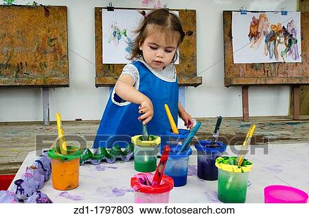 A little girl wears a blue apron uses a paintbrush and paint to paint a picture View Large Photo Image Stock Image - A little girl wears a blue apron uses a paintbrush and paint to paint a picture. Fotosearch