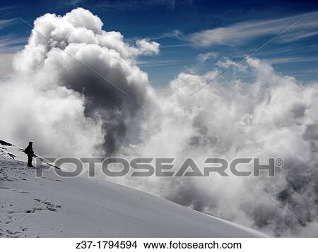 Picture - A lone climber stands on fresh snow near the top of Mount Kilimanjaro at 5900 meters 19000 feet above sea level as a bank of clouds rises above the ridge. Fotosearch