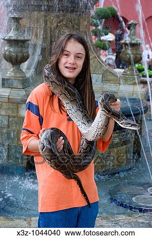 Stock Image - A long haired boy poses for s photo holding a python in Malacca Malaysia. Fotosearch