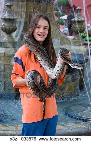 Stock Photograph - A long haired boy poses for s photo holding a python in Malacca Malaysia. Fotosearch