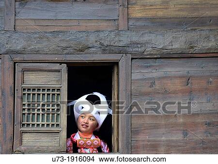 Picture - A Long Horn Miao girl looking out the window of her home. Fotosearch
