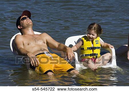 Stock Image - A man, 20-30, and a little girl cool off sitting in chairs in a lake.. Fotosearch