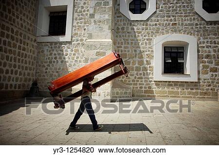 Stock Image - A man carries a church bench to the Basilica de la Soledad, or Solitude Basilica, after a holy week procession in Oaxaca, Mexico. Fotosearch