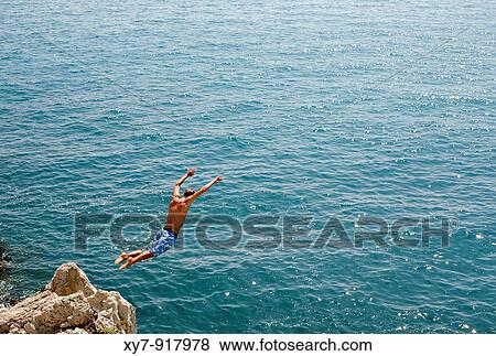 Stock Photo - A man dives off a cliff into the sea at Antibes on the Cote D? Azur in southern France. Fotosearch