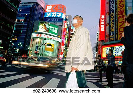 A man, filtering out pollution with his mask, crosses the street beneath a rainbow of neon at dusk in Shinjuku. Tokyo. Japan View Large Photo Image Stock Photo - A man, filtering out pollution with his mask, crosses the street beneath a rainbow of neon at dusk in Shinjuku. Tokyo. Japan. Fotosearch