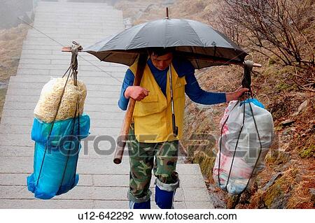 Stock Image - A man is cary food up to the mountain of Huang - shan. It will take him up to 9 hours. Those mountains are also called yellow mountains by the chinese people.. Fotosearch