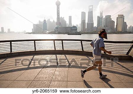 Stock Photo - A man jogs early morning on the Bund against the skyline of modern Shanghai, China.. Fotosearch