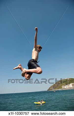 Stock Photo - A man jumping into the sea, Aberystwyth seaside resort, wales UK, summer afternoon. Fotosearch