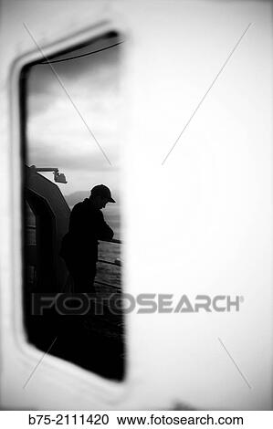 A man leaning on the railing of a boat at looking at the sea, reflected in a window. Croosing the Mediterranean Sea from Ciutadella, Menorca to Alcudia, Mallorca, Balearic Islands, Spain View Large Photo Image Stock Image - A man leaning on the railing of a boat at looking at the sea, reflected in a window. Croosing the Mediterranean Sea from Ciutadella, Menorca to Alcudia, Mallorca, Balearic Islands, Spain. Fotosearch