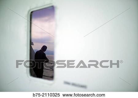 A man leaning on the railing of a boat at looking at the sea, reflected in a window. Croosing the Mediterranean Sea from Ciutadella, Menorca to Alcudia, Mallorca, Balearic Islands, Spain View Large Photo Image Stock Photography - A man leaning on the railing of a boat at looking at the sea, reflected in a window. Croosing the Mediterranean Sea from Ciutadella, Menorca to Alcudia, Mallorca, Balearic Islands, Spain. Fotosearch