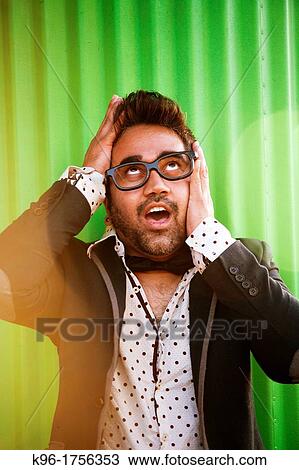 Stock Image - A man making an exaggerating facial expression with hands on his face in a funny manner. Fotosearch