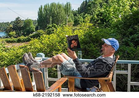 Stock Photo - a man reads on the deck of Breezy Bay bed and breakfast, Saturna Island, Gulf Islands, British Columbia, Canada.. Fotosearch
