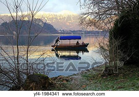 A man rowing a Pletna, a covered wooden rowing boat, on Lake Bled Slovenia. View Large Photo Image Stock Image - A man rowing a Pletna, a covered wooden rowing boat, on Lake Bled Slovenia.. Fotosearch