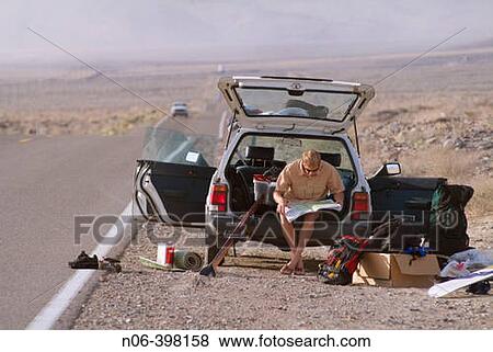 Stock Photo - A man sitting on tailgate of car in the desert. Fotosearch