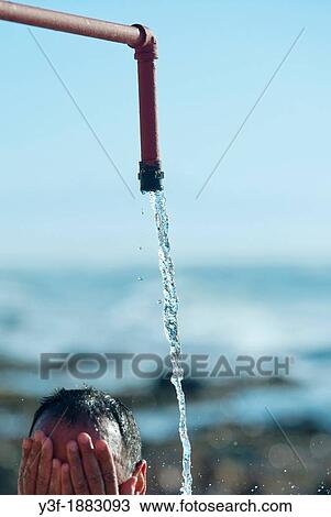 Stock Image - A man stands under a freshwater shower at the beach Washing the sea salt off his body. Fotosearch