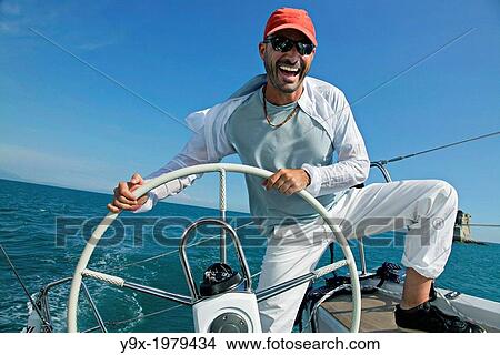 A man steers a sailboat on the open ocean against a bright blue sky in Italy. View Large Photo Image Picture - A man steers a sailboat on the open ocean against a bright blue sky in Italy.. Fotosearch