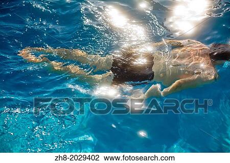 A man underwater swimming as sunlight reflects off the bright blue water. View Large Photo Image Stock Image - A man underwater swimming as sunlight reflects off the bright blue water.. Fotosearch