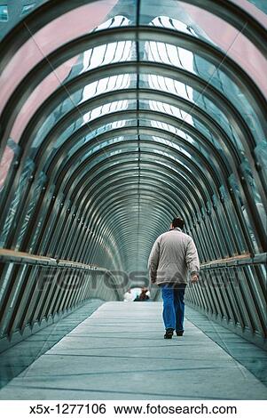 Stock Photograph - A man walks alone through the tunnel of a covered skybridge in La Defense, Paris, France. Fotosearch