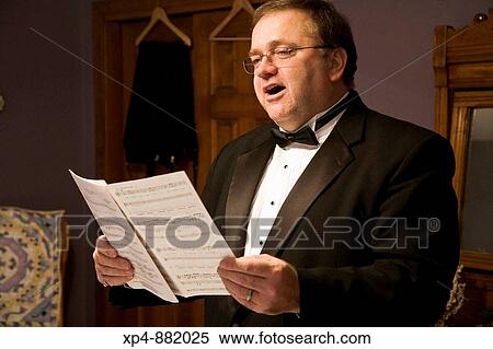 A man wearing a black tuxedo and bow tie singing from a book of sheet music in his dressing room. View Large Photo Image Stock Photography - A man wearing a black tuxedo and bow tie singing from a book of sheet music in his dressing room.. Fotosearch
