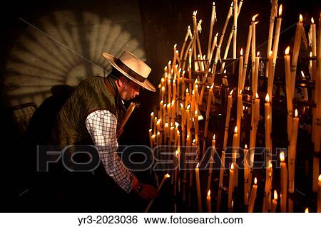Stock Photograph - A man, wearing a Spanish hat, lights candles at the Votive Room of the shrine of the Virgin of Rocio, in Almonte, Donana National Park, Huelva province, Andalusia, Spain. Fotosearch