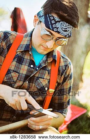 A man wearing suspenders, flannel, and a bandana sharpens a maul View Large Photo Image Stock Photo - A man wearing suspenders, flannel, and a bandana sharpens a maul. Fotosearch