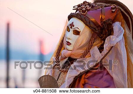 Stock Photo - A masked woman at the pier at sunrise at the carnival in Venice, Italy, Europe. Fotosearch