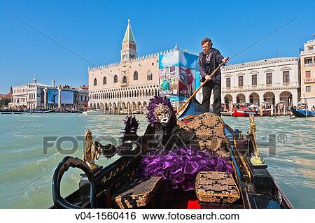 Stock Photograph - A masked woman in a gondola with the Palazzo Ducale in the background at the carnival in Venice, Italy, Europe. Fotosearch