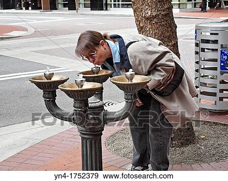 Stock Photo - A mature woman drinks from a fountain on a downtown sidewalk in Portland, Oregon. Fotosearch