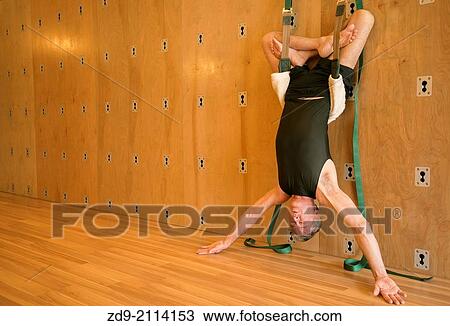 Stock Image - A middle-aged man demonstrates an ashtanga yoga pose on the yoga wall.. Fotosearch