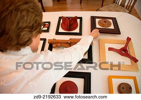 Stock Image - A middle aged woman shows off her artistic project of mounted wooden objects.. Fotosearch
