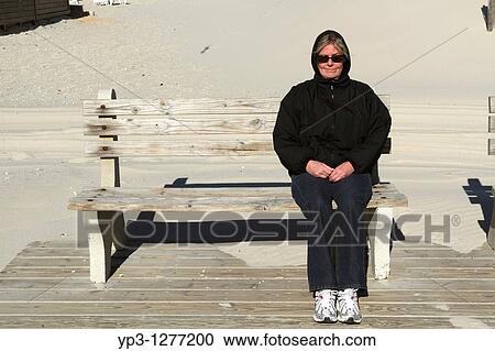 A middle-aged woman sitting on a wooden bench at the end of a seaside boardwalk smiling Fall/Winter Lavalette, New Jersey, USA View Large Photo Image Stock Image - A middle-aged woman sitting on a wooden bench at the end of a seaside boardwalk smiling Fall/Winter Lavalette, New Jersey, USA. Fotosearch