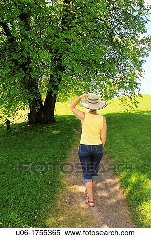 Stock Photography - a middle aged woman walking along a path through trees in a field during spring. Fotosearch