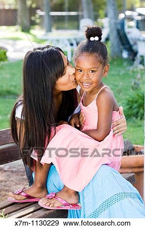 A mixed race mother kisses her smiling daughter on the cheek View Large Photo Image Stock Photo - A mixed race mother kisses her smiling daughter on the cheek. Fotosearch