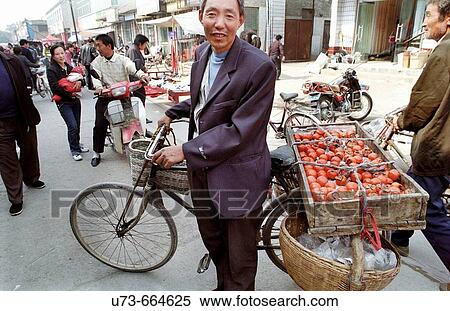 Stock Photography - A mobile fruit vendor sells his Persimons in a local weekly market in a small town in south Shanxi province, China. Fotosearch