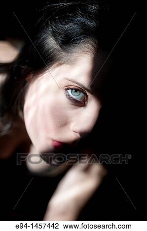 Stock Image - A moody, shadowy portrait of a nineteen year old brunette woman, looking at the camera, one eye visible. Fotosearch