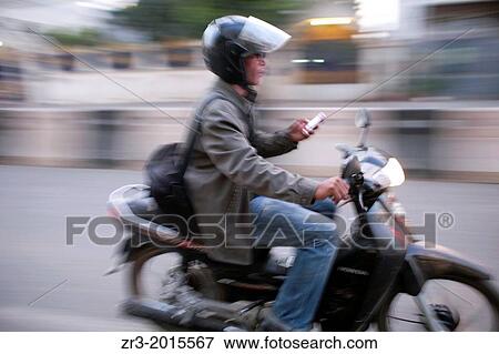 Stock Photo - A motorcycle rider checks his smartphone in Phnom Penh, Cambodia.. Fotosearch