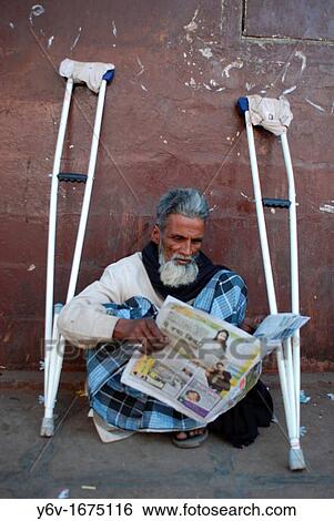 Stock Photograph - A muslim man with crutches is reading the newspaper in a street at Bombay, India.. Fotosearch