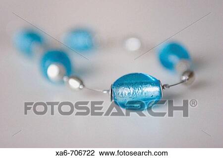 A necklace consisting of large blue glass beads on a silver wire. One bead is in focus in the foreground and the rest fall out of focus on the light grey background. View Large Photo Image Stock Image - A necklace consisting of large blue glass beads on a silver wire. One bead is in focus in the foreground and the rest fall out of focus on the light grey background.. Fotosearch
