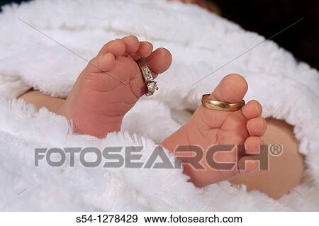 Stock Photo - A newborn baby's feet, with the parents? wedding rings on his toes. Fotosearch