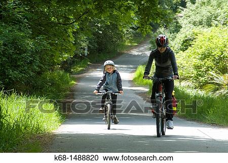 Stock Image - a nine year old boy and a middle-aged woman ride bicycles on a country road on Saltspring Island, Gulf Islands, BC, Canada. Fotosearch