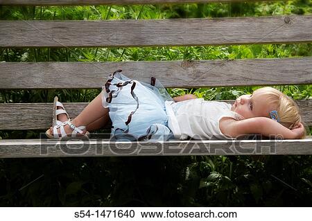 Stock Image - A one-year-old caucasian girl lying on a bench.. Fotosearch