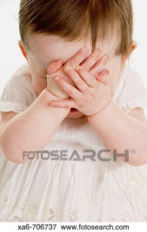 A one-year-old girl wearing a white dress clasps her hands over here face. View Large Photo Image Stock Photo - A one-year-old girl wearing a white dress clasps her hands over here face.. Fotosearch