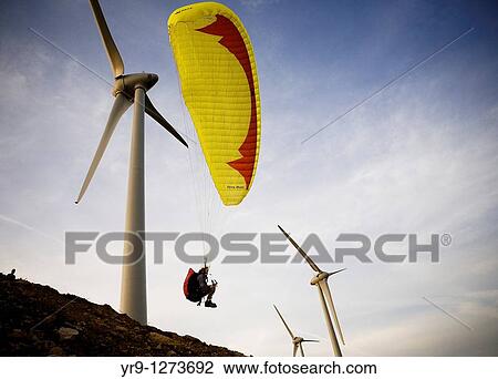 Stock Image - A paraglider is taking off in between the wind turbines, what would be totally insane if these would be in service: It was while the installation of this windfarm As it is in service now, this take of in not usable anymore La Pea Hill, Tarifa, Spain. Fotosearch