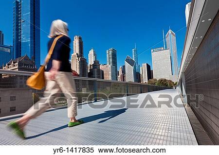 Stock Photography - A pedestrian walks the Nichols Bridgeway with the Skyline of Chicago from Millennium Park in Chicago, IL, USA. Fotosearch