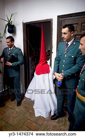 A penitent wearing a red pointed hood and a white cape pass by Guardia Civil members, a Spanish military-status police force inside a church as he waits the start of an Easter Holy Week procession in Carmona, Seville province, Ansalusia, Spain View Large Photo Image Picture - A penitent wearing a red pointed hood and a white cape pass by Guardia Civil members, a Spanish military-status police force inside a church as he waits the start of an Easter Holy Week procession in Carmona, Seville province, Ansalusia, Spain. Fotosearch
