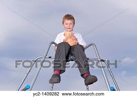 Stock Image - A picture of a seven year old boy and his cuddly toy outdoors on a climbing frame in the Uk. Fotosearch